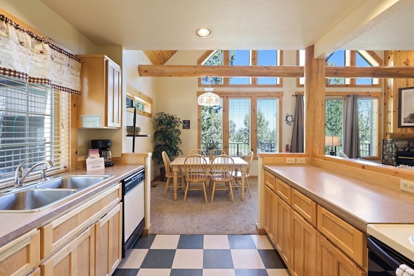 A kitchen with wooden cabinets, a checkered floor, a dining area with chairs, and large windows.