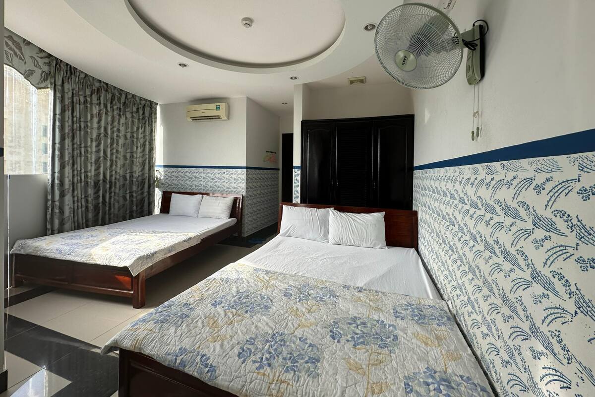 A hotel room with two single beds, a ceiling fan, an air conditioning unit, and a patterned wall.