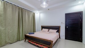 A bedroom with a bed, curtains, a door, and a ceiling light fixture.