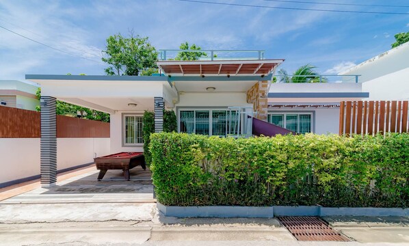 A modern house with a covered patio, a pool, and a well-maintained garden.