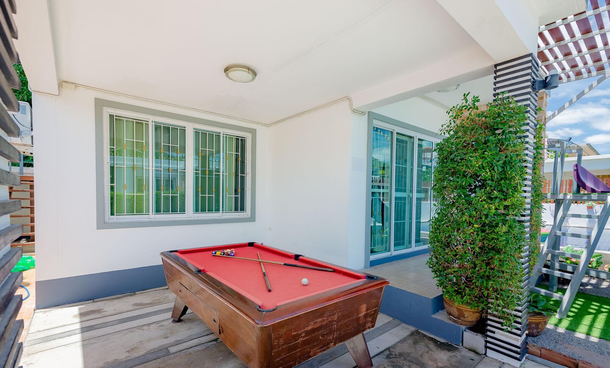 A pool table with balls, a window, and a plant.