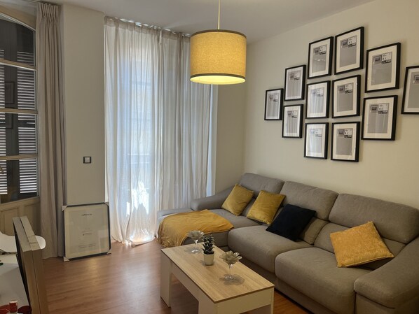 Uma sala de estar moderna com um sofá, uma mesa de centro e uma grande janela com cortinas leves.