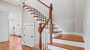 Un escalier avec des marches en bois et des rampes blanches, menant à un palier où se trouvent un panier et une porte.
