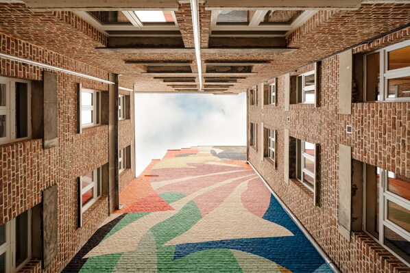 A corridor with brick walls, windows, and a colorful patterned floor. - Edgar Suites Lille - Faidherbe (Lille)