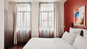 Een hotelkamer met een bed, gordijnen, een radiator, een lamp en een schilderij aan de muur.