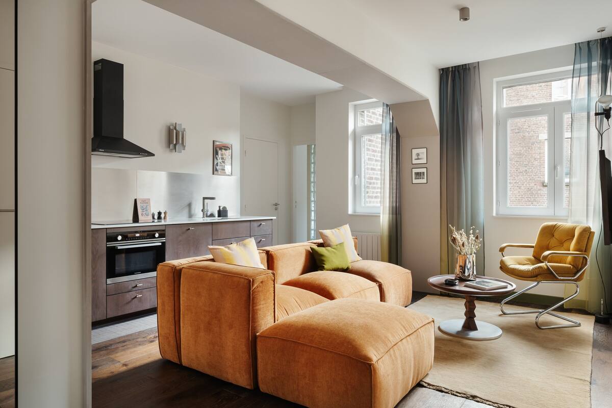 A modern living room with a sofa set, a dining table with a vase, and a kitchen in the background.