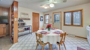 A dining area with a round table set for four, wooden chairs, a ceiling fan, and a kitchen area with a microwave and refrigerator. - Mason Cabin w/ Private Dock on Marengo Lake! (Mason)