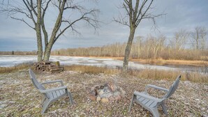 A bench seating area with a fire pit in the center, surrounded by leaf-covered ground and trees. - Mason Cabin w/ Private Dock on Marengo Lake! (Mason)