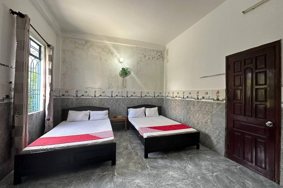 A room with two beds, a wooden door, and a window with curtains.
