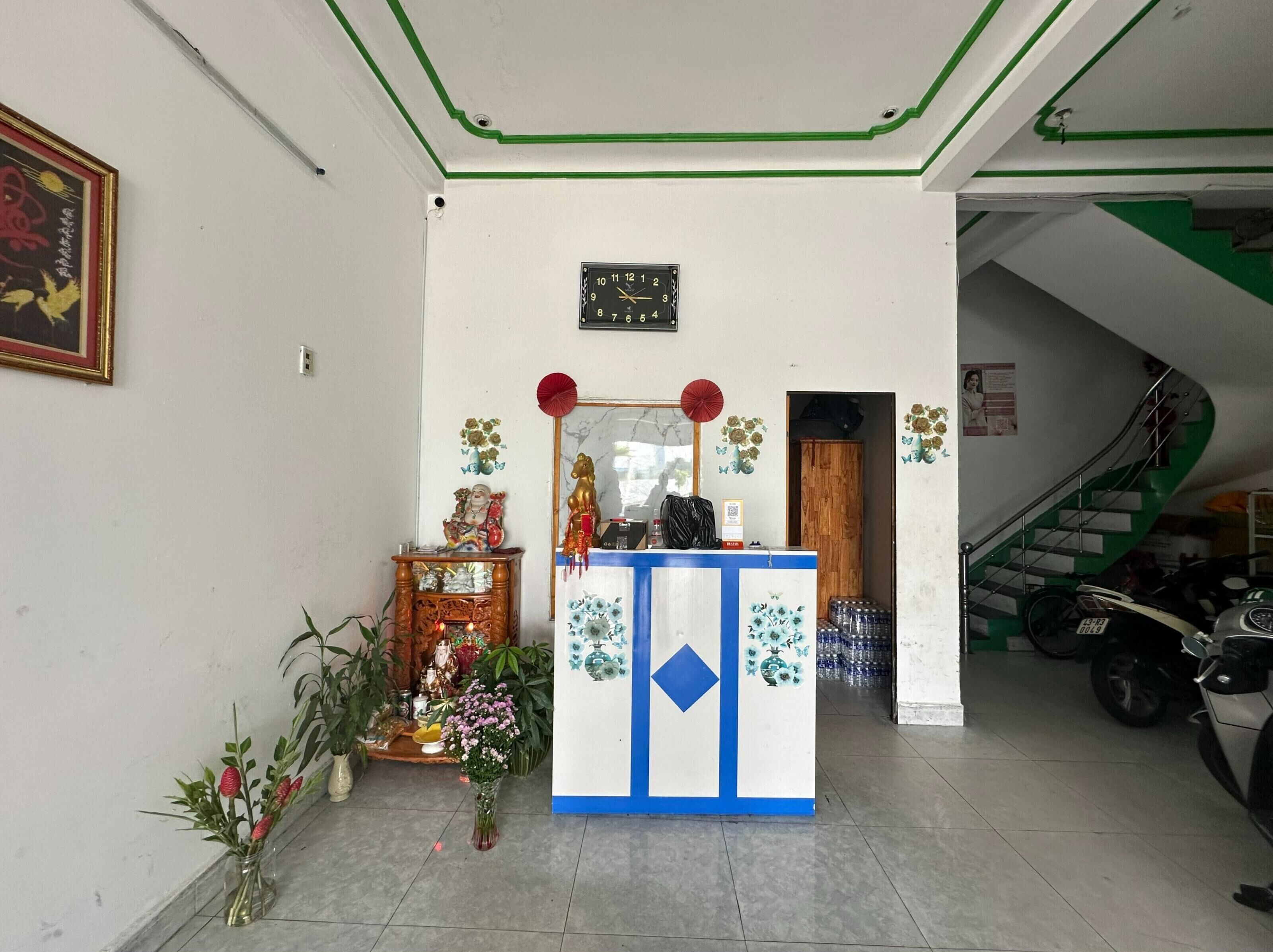 Ein Empfangsbereich mit einer Uhr, einem kleinen Altar mit religiösen Figuren und einer Treppe, die in eine andere Etage führt.