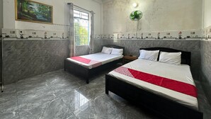 Habitación de hotel con dos camas, una ventana con cortinas, aire acondicionado de pared, ventilador de techo y una estantería decorativa con objetos pequeños.