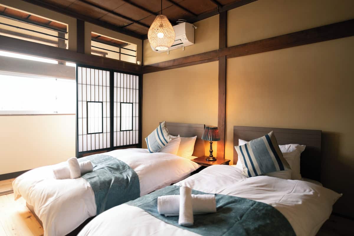 A hotel room with two beds, a wooden ceiling, a window with bars, and a hanging light fixture.