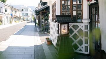 A street view of a building with a white facade, a wooden door, and a small signboard.