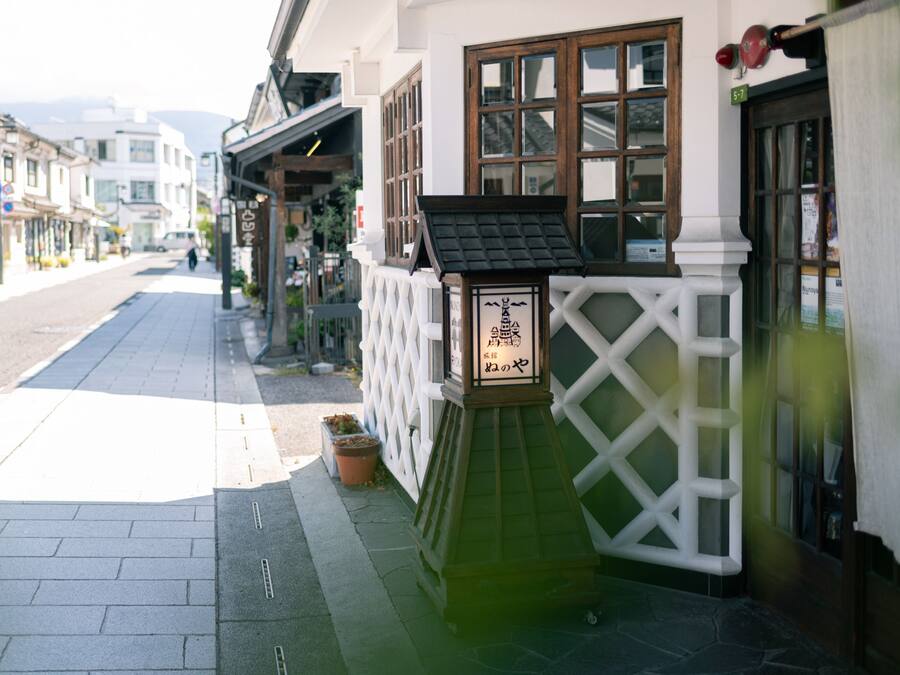 A street view of a building with a white facade, a wooden door, and a small signboard.