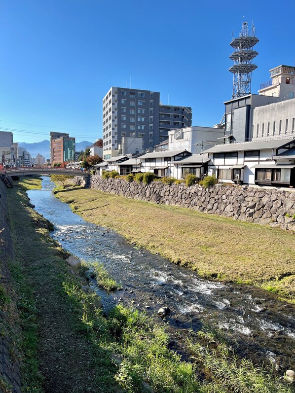 A river flowing through a grassy area with buildings in the background. - Nunoya Ryokan (Matsumoto)