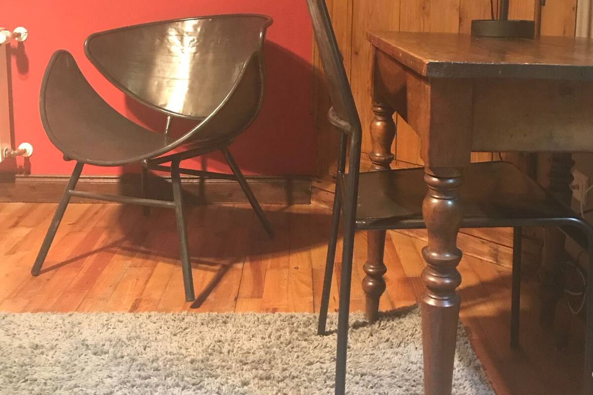 Et værelse med rød væg, et træskab, et metalbord, en træstol og en gulvlampe i metal.