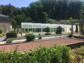 Une serre avec une piscine, entourée de haies et de plantes bien entretenues.