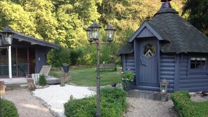 A rustic wooden cabin with a thatched roof, a gravel pathway leading to it, and a statue in the foreground. - Domaine du Moulin (Saint-Avold)