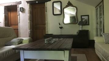 A living room with a wooden table, two sofas, a wooden door, and a mirror.