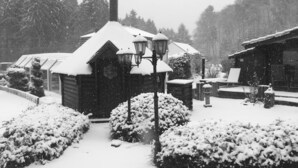 A snow-covered cabin with a chimney, a wooden porch, and a snow-covered landscape. - Domaine du Moulin (Saint-Avold)