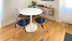 Een eetgedeelte met een ronde tafel en vier stoelen, een televisie aan de muur en een plant op een kast.