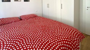 Een slaapkamer met een bed voorzien van rood beddengoed met stippen, witte kasten en een plafondlamp.
