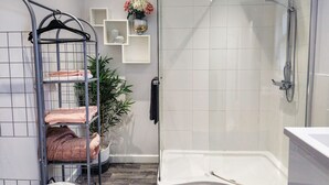 Une salle de bain moderne dotée d’une douche à parois de verre, d’une baignoire intégrée et d’un porte-serviettes en métal sur lequel sont pliées des serviettes.