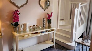A hallway with a white console table, two mirrors, and a staircase.