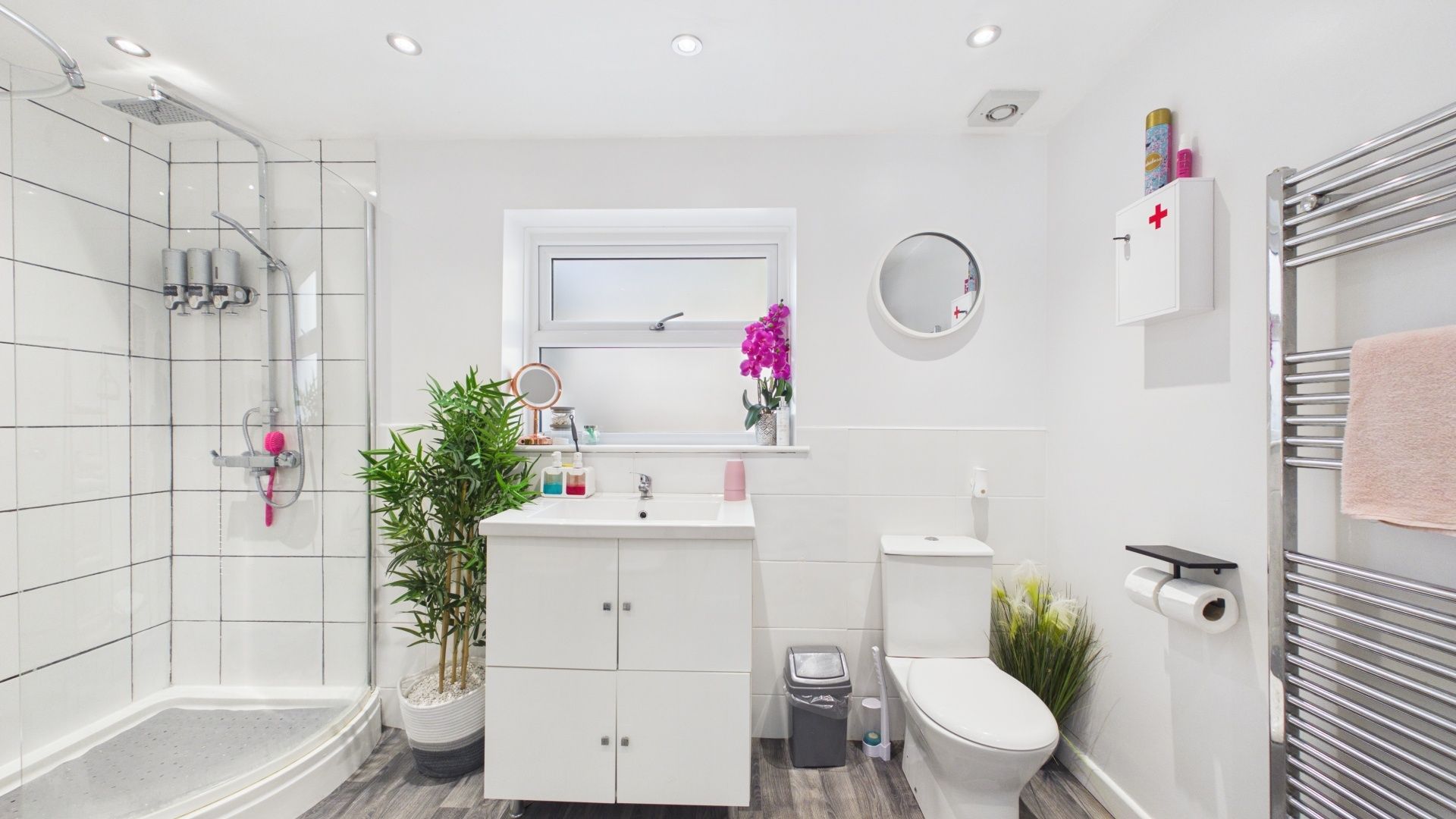 A modern bathroom with a shower, toilet, sink, and a small window.