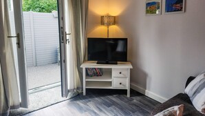 A room with a television on a white desk, a bookshelf, a lamp, and a door leading to an outdoor area.