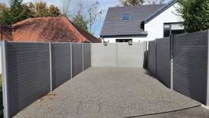 A gated driveway leading to a house with a grey roof and white walls.