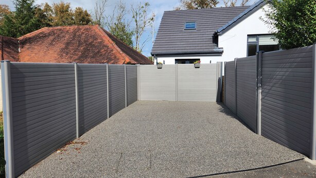 Une allée fermée par un portail mène à une maison avec un toit gris et des murs blancs.