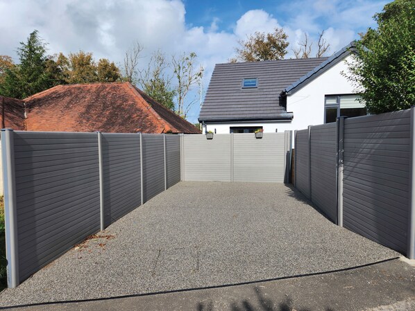 Ein von einer Mauer gesäumter Weg führt zu einem Haus mit grauem Dach und weißen Wänden.