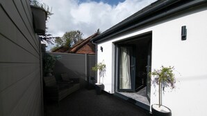 Un petit espace extérieur clos, comprenant une terrasse, une porte-fenêtre coulissante et deux plantes en pot.