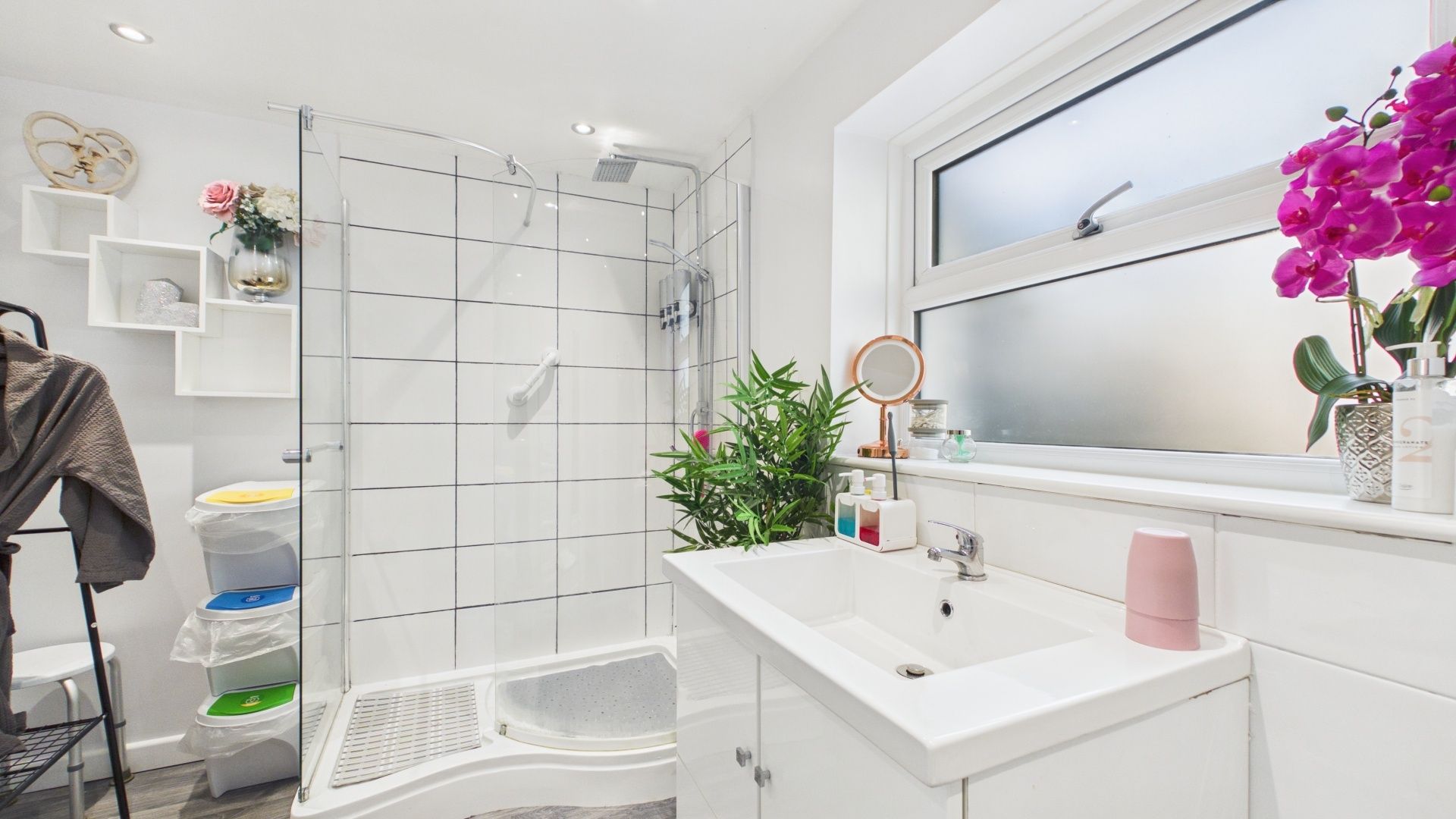 Un baño moderno con cabina de ducha de vidrio, lavamanos blanco y ventana con vistas.