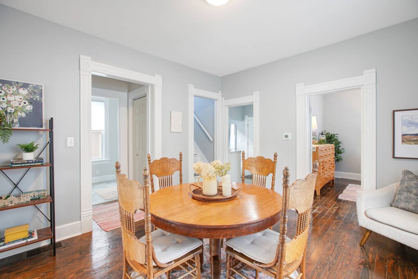 A dining area with a round wooden table, six chairs, and a central vase with flowers.