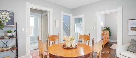 A dining area with a round wooden table, six chairs, and a central vase with flowers.