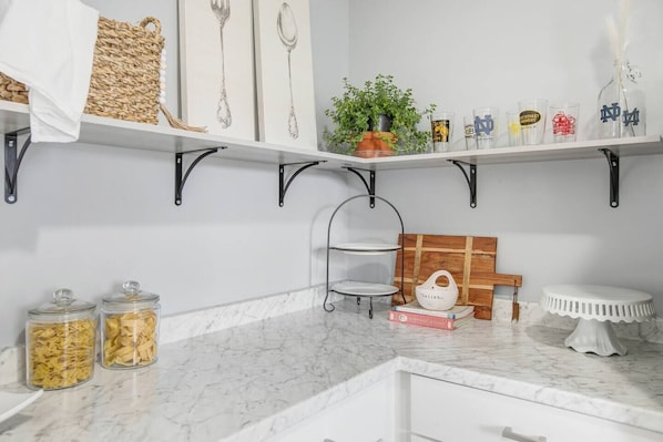Una cocina con encimeras de mármol blanco, estantes de metal negro y diversos utensilios de cocina.