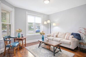 Un salon comprenant un canapé, une table basse et des fauteuils, une fenêtre avec des stores et une lampe.