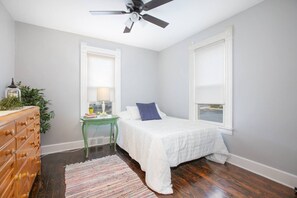 A bedroom with a bed, dresser, nightstand, lamp, and a view of the outdoors.