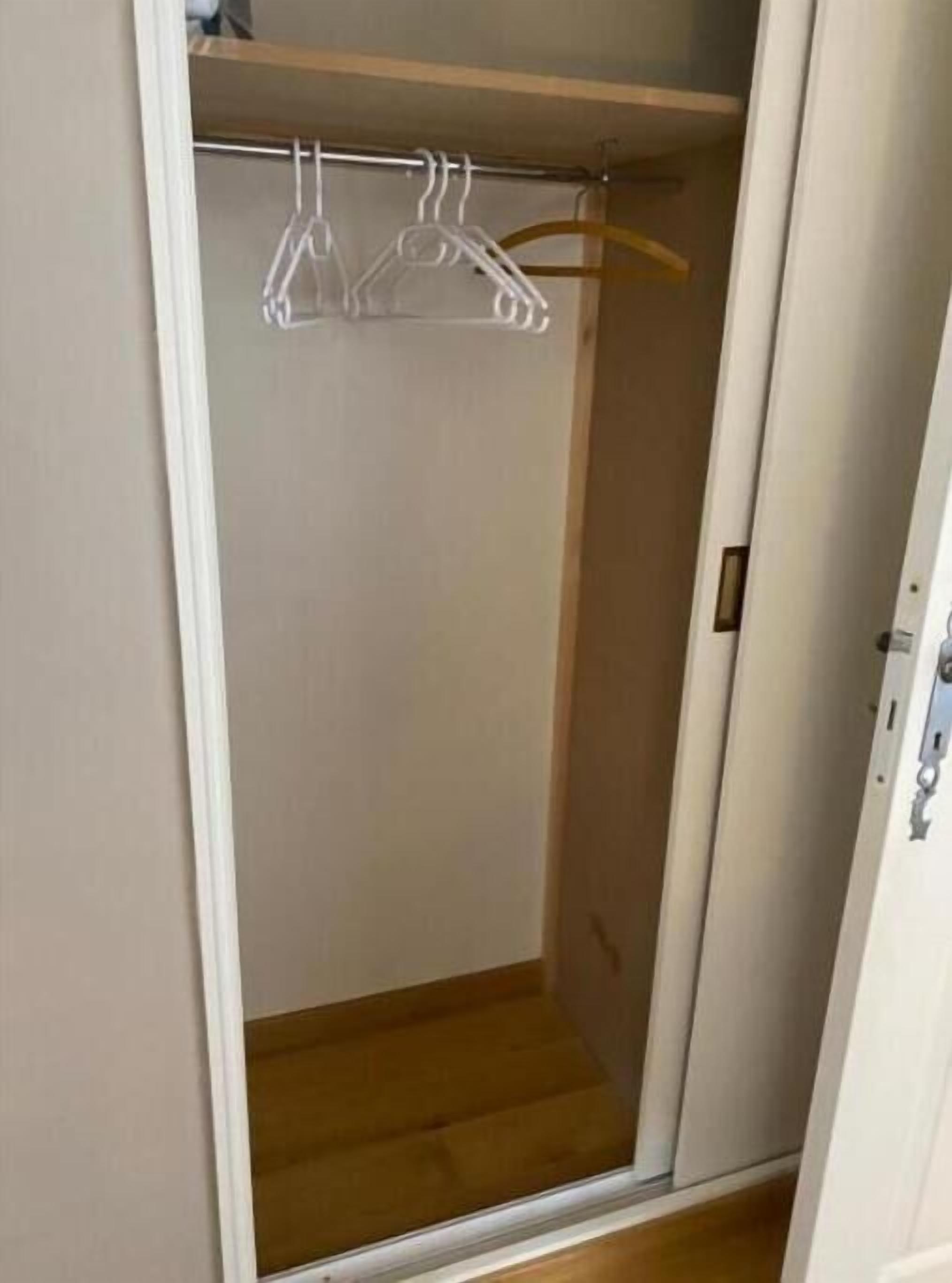 Un vestidor con piso de madera, paredes blancas y una barra de metal con perchas.