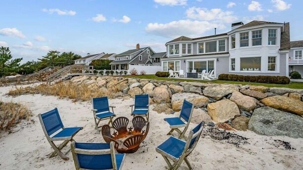 Une propriété située en bord de mer, dotée d’un mur en pierre, de chaises de plage bleues et d’un foyer extérieur.