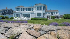 Une maison à deux étages dotée d’une baie vitrée, d’un porche couvert et d’un mur de pierre en premier plan.