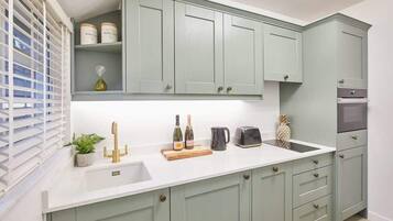 A kitchen with light green cabinets, a white countertop, a sink, and a window with blinds.