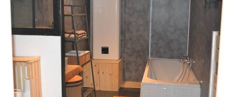 Une salle de bain avec une baignoire, des toilettes, une étagère avec des serviettes et un réfrigérateur blanc.
