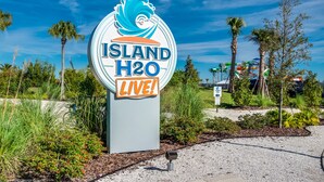 Une enseigne pour Island H2O, avec un logo représentant une vague, entourée de verdure et de palmiers.