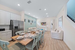 A modern kitchen with white cabinets, a stainless steel refrigerator, and a dining area with a wooden table set for four.