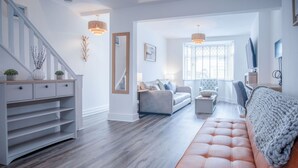 A modern living room with a staircase, a grey sofa, a brown leather ottoman, and a wooden coffee table. - Castle Square - 2 Bedroom - Mumbles (Swansea)
