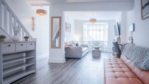 A modern living room with a grey sofa, a brown leather couch, and a wooden cabinet with plants. - Castle Square - 2 Bedroom - Mumbles (Swansea)