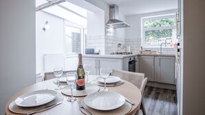 A modern kitchen with white cabinets, a gas stove, and a window overlooking a garden. - Castle Square - 2 Bedroom - Mumbles (Swansea)